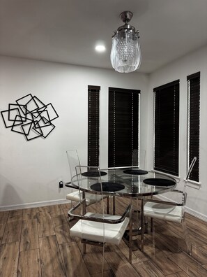 A dining area with a glass table, chairs, and a chandelier.