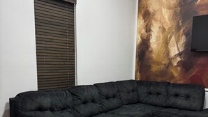 Una sala de estar moderna con un sofá modular, una mesa de centro redonda de vidrio, un sillón rojo y un cuadro abstracto grande en la pared.