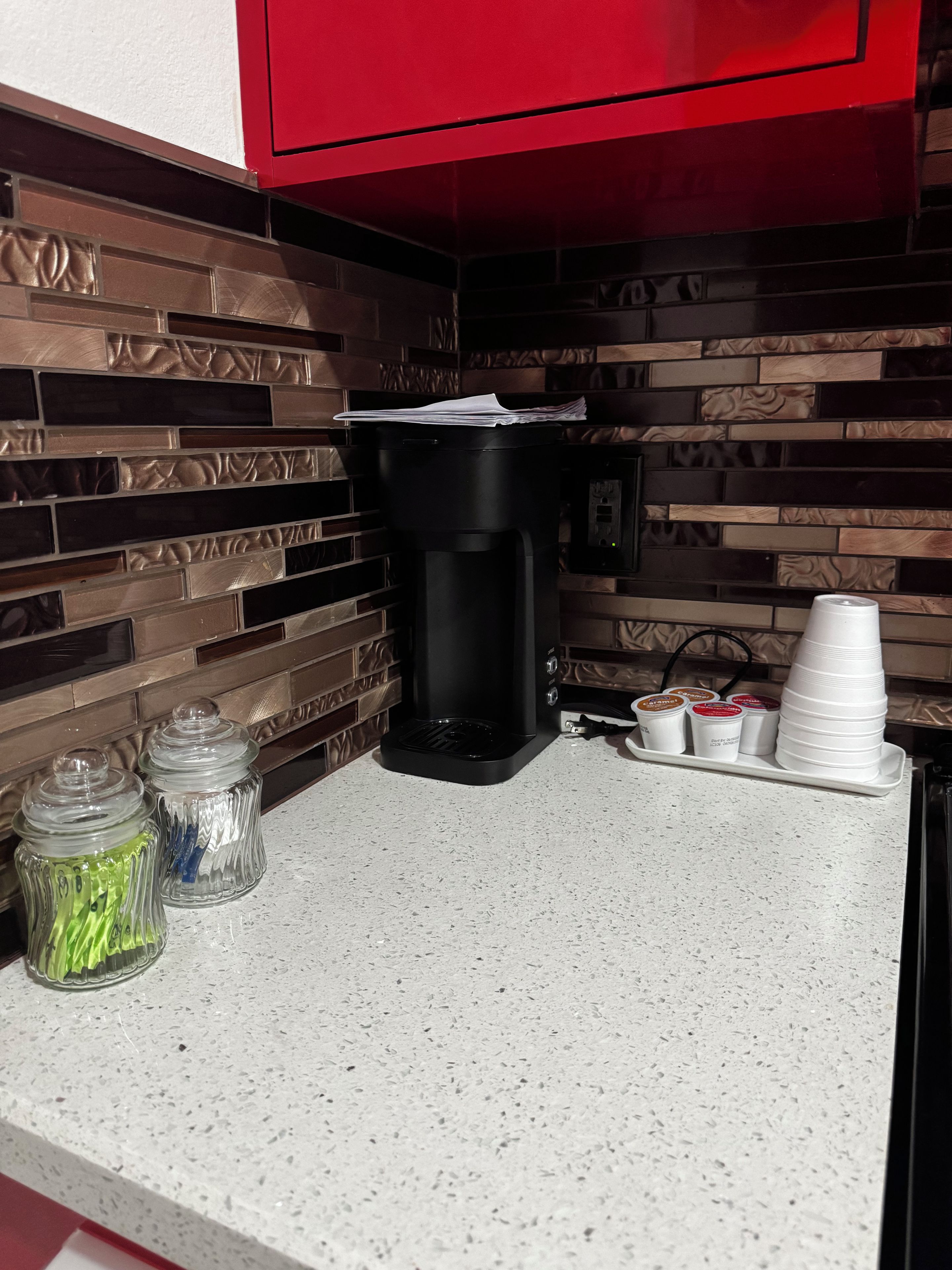 Un comptoir de cuisine avec une machine à café, une pile de gobelets en papier et deux bocaux en verre.