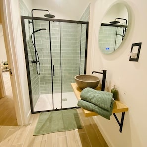 A bathroom with a glass-enclosed shower, a round mirror, a wooden vanity, and a green towel. - Devon Countryside Retreat Near Exeter (Newton Saint Cyres)