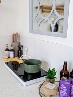 Una cocina con estufa, una olla verde, una planta pequeña y algunas botellas.
