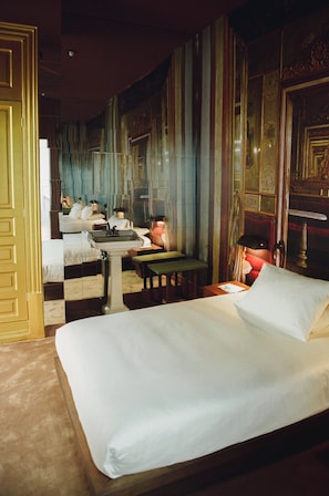 Quarto de hotel com cama, escrivaninha, cadeira, espelho e janela.