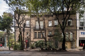 Un edificio de varios pisos con fachada tradicional, ventanas amplias y un árbol en la entrada.