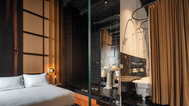 A modern hotel room with a large bed, a glass partition, a bathroom with a sink and toilet, and a mirror. - Casa Bosques Pensión (Mexico City)