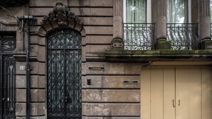 A building facade with a black ornate gate, a beige door, and a balcony with a wrought iron railing. - Casa Bosques Pensión (Mexico City)