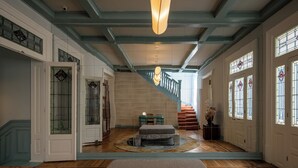 A spacious hallway with a staircase, a stone bench, and a large chandelier. - Casa Bosques Pensión (Mexico City)