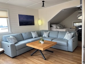 Una sala moderna con un sofá modular, una mesa de centro de madera y una cama al fondo.