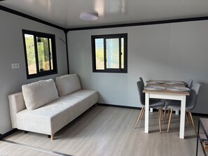 A modern room with a sofa, a dining table with chairs, and two windows with black frames. - New: Enjoy a peaceful vacation in Corsica (Tavaco)