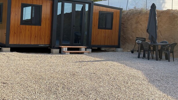 Un bâtiment moderne à structure modulaire, doté de panneaux extérieurs en bois, de grandes portes vitrées et d’un sol en gravier.