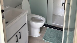 Une salle de bain comprenant des toilettes, un lavabo, une douche en verre et une porte dotée d’une poignée.