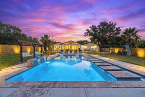 A swimming pool with lounge chairs, a covered seating area, and a sunset sky. - Modern Copano Bayfront Retreat – Pool & Private Lighted Pier | Sleeps 8 (Rockport)