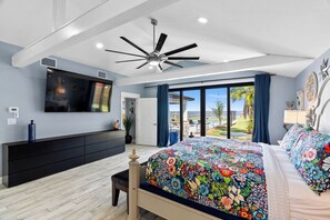Ein Schlafzimmer mit einem großen Bett, einem Deckenventilator, einem Fernseher und Blick ins Freie.