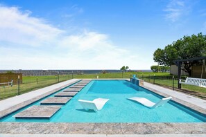 Ein rechteckiger Pool mit klarem, blauem Wasser, umgeben von einer Steindeck und einem Metallzaun.