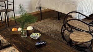 A room with a bed, a wooden table with a vase, a bowl, and a remote control.