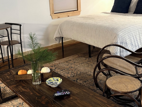 Una habitación con una cama, una mesa de madera con un jarrón, un cuenco y un control remoto.