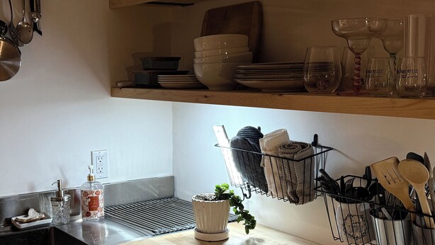 A kitchen with a wooden countertop, a sink, a dish rack, and various kitchen utensils.
