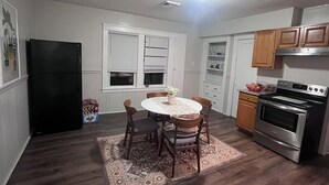 A compact kitchen with a dining table, chairs, a refrigerator, oven, and wooden cabinets. - Spacious 5-bedroom apartment (Worcester)