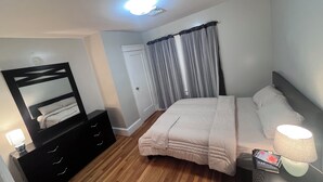 A bedroom with a bed, a dresser, a mirror, a door, and a window with curtains. - Spacious 5-bedroom apartment (Worcester)