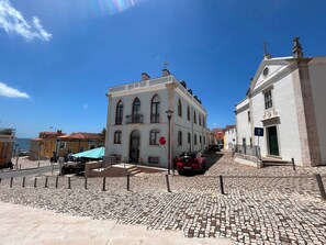 Une rue pavée bordée de bâtiments historiques, un ciel bleu dégagé et une voiture garée.