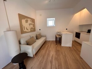 Ein gemütlicher Wohnraum mit einer Couch, einem kleinen Tisch, einer Küchenzeile und einem Fenster.