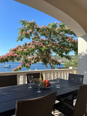 A table with chairs, a bottle, and fruit on a balcony overlooking a body of water and a boat. - 2-bedroom apartment in fabulous Sevid na moru with AC (Sevid na moru)