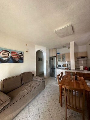 A living room with a sofa, a dining table with chairs, a kitchen area with cabinets and appliances, and a painting on the wall. - 2-bedroom apartment in fabulous Sevid na moru with AC (Sevid na moru)