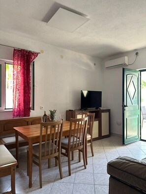 A dining area with a wooden table and chairs, a television on a stand, and a door leading outside. - 2-bedroom apartment in fabulous Sevid na moru with AC (Sevid na moru)