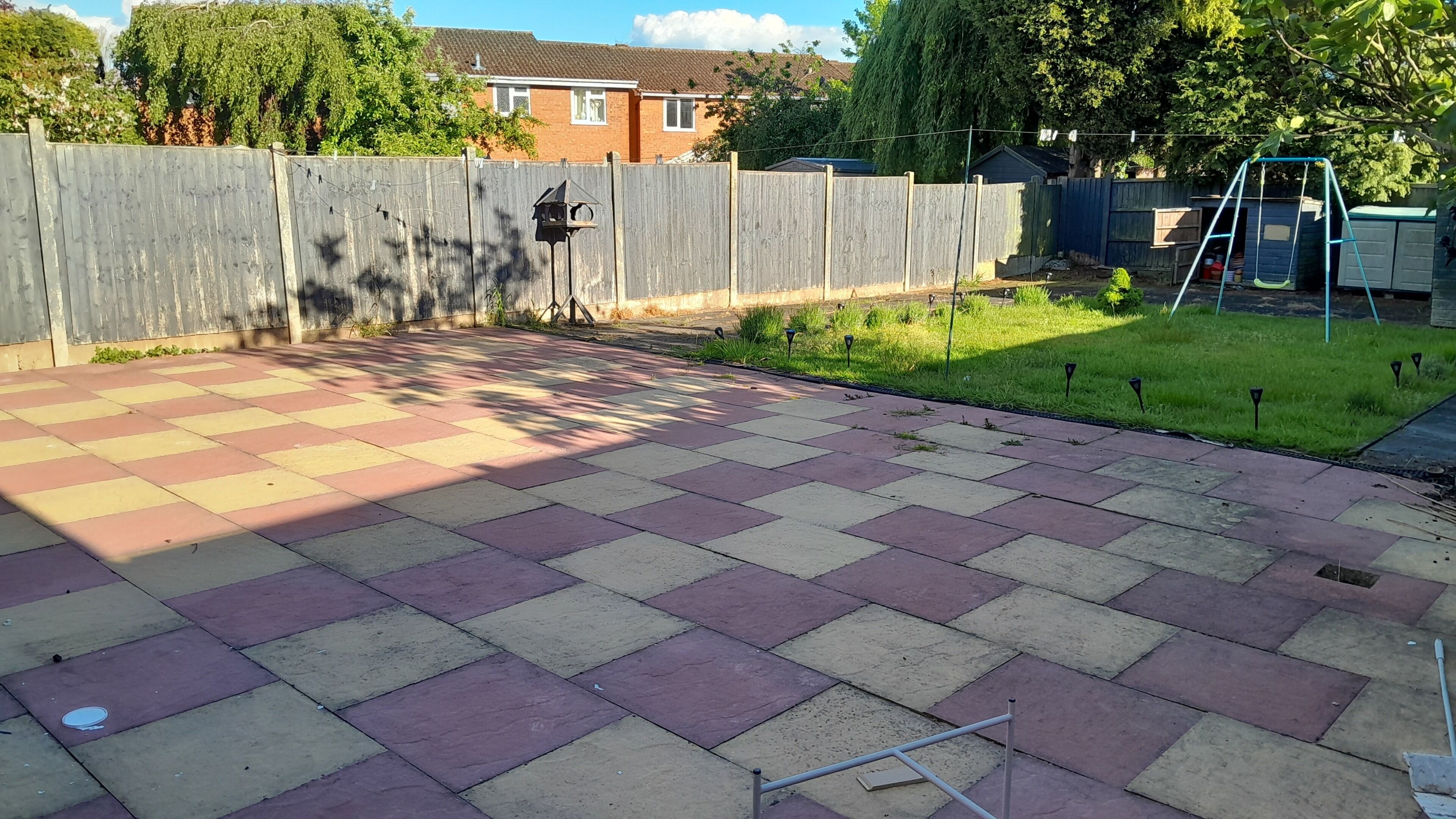 A paved patio with a checkered pattern, a wooden fence, and a grassy area with a swing set.