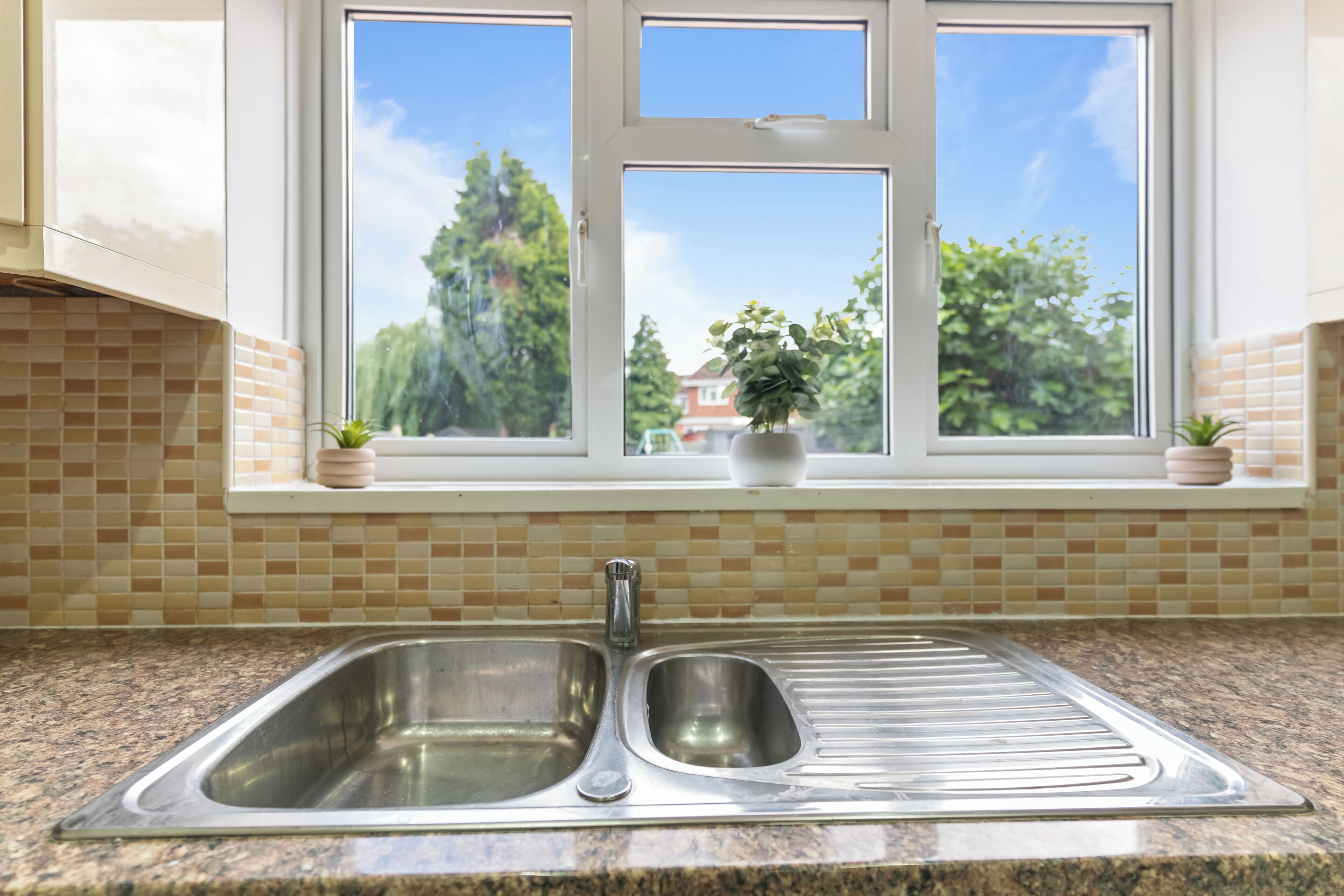 A kitchen with a double stainless steel sink, a window with a view of trees, and a tiled backsplash.