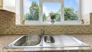 A kitchen with a double stainless steel sink, a window with a view of trees, and a tiled backsplash. - Modern 5 Bed Fully Detached Guest House (with parking) (Walsall)