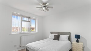 A bedroom with a bed, a nightstand, a ceiling fan, a window with blinds, and a radiator. - Modern 5 Bed Fully Detached Guest House (with parking) (Walsall)