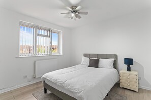A bedroom with a bed, a nightstand, a ceiling fan, a window with blinds, and a radiator. - Modern 5 Bed Fully Detached Guest House (with parking) (Walsall)