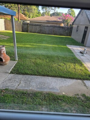 A well-maintained lawn with a wooden fence, a patio area, and a house in the background. - Spacious 5-bedroom 2 bath newly renovated house in beautiful Seabrook, new AC. (Seabrook)