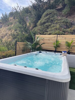 Ein Whirlpool mit Holzterrasse, umgeben von Grünpflanzen und einem Holzzaun.