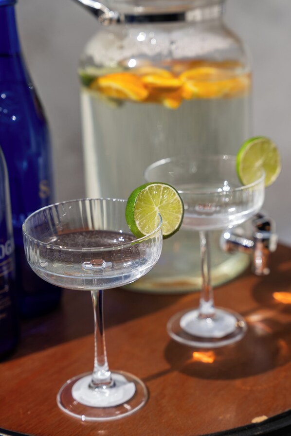 Deux verres transparents garnis de rondelles de citron vert, une carafe remplie de fruits et une bouteille bleue.