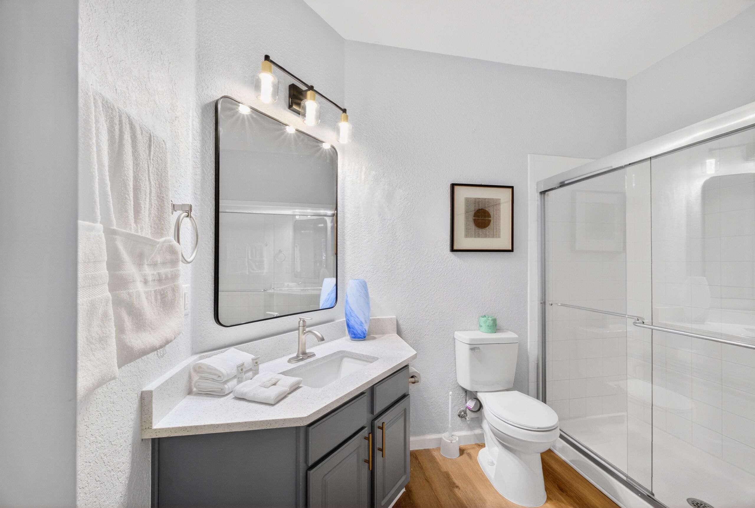 Un baño moderno con lavamanos, espejo, inodoro y cabina de ducha de vidrio.