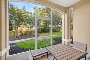 Eine überdachte Terrasse mit Tisch und Bank, großen Fenstern und Blick auf einen angelegten Garten.