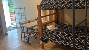 Un lit superposé avec une couvre-lit à motifs géométriques, une table en bois avec une chaise et une étagère en métal.