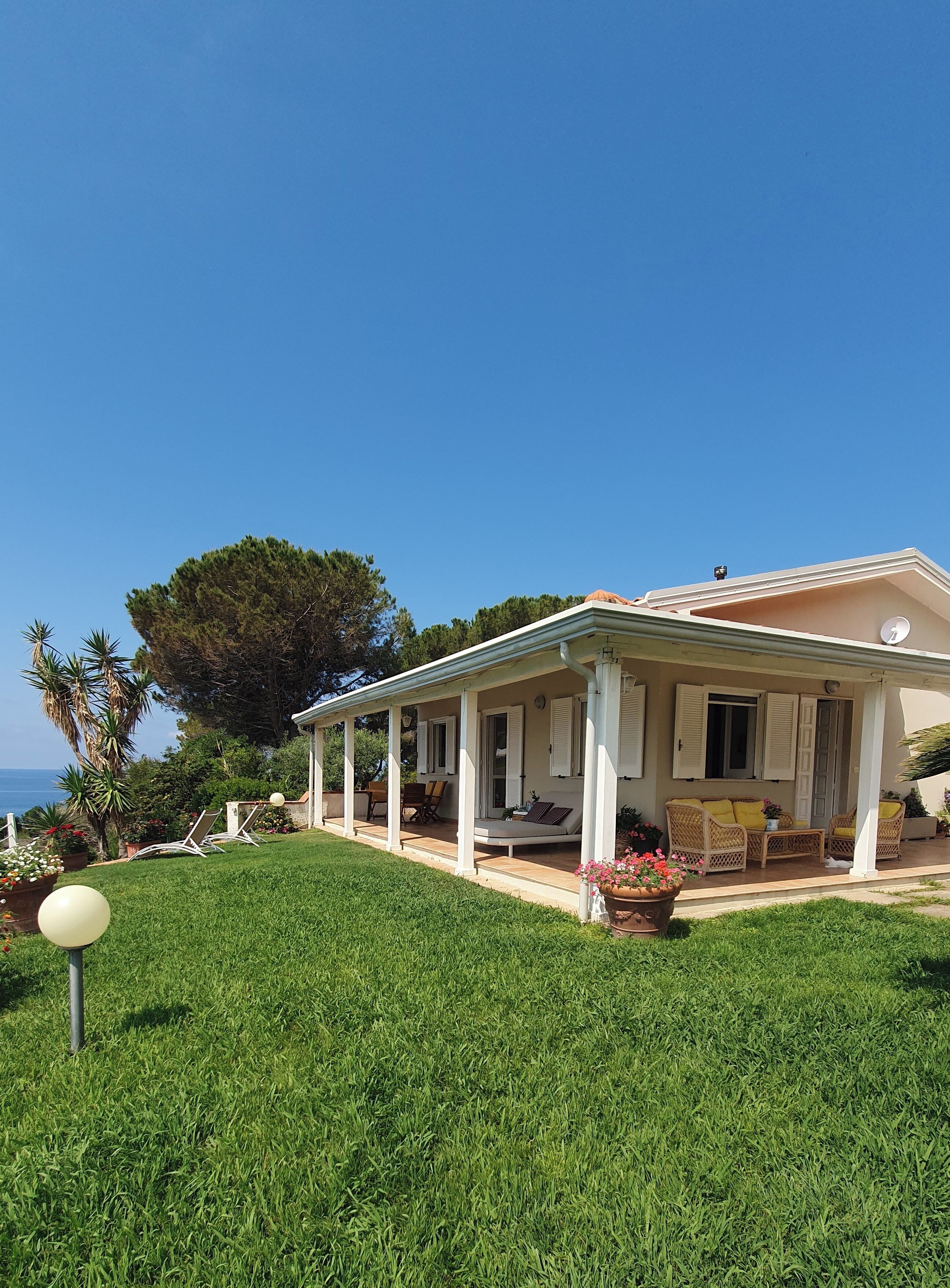Una casa con porche cubierto, mobiliario exterior y vista al mar.