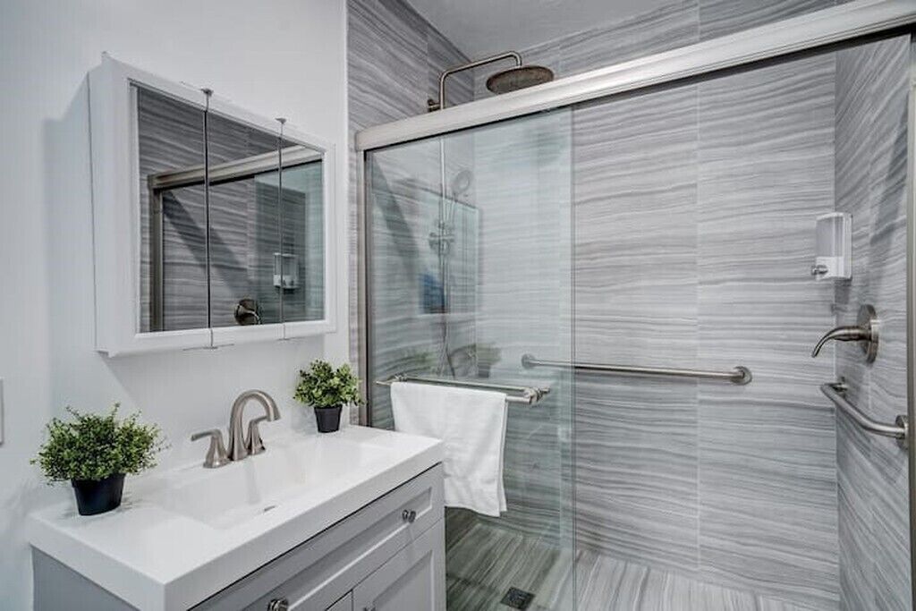 Un baño moderno con cabina de ducha de vidrio, un tocador blanco con espejo y un perchero para toallas.