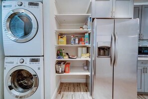 Ein Waschraum mit Waschmaschine, Trockner und Kühlschrank. Regale mit verschiedenen Gegenständen.