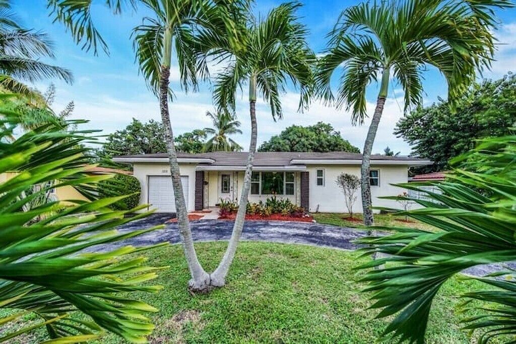 A single-story house with a front porch, surrounded by palm trees and a well-maintained lawn.