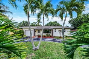 Einbungalow mit Veranda, umgeben von Palmen und einem gepflegten Rasen.
