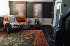 A living room with a leather sofa, a patterned rug, a wood-burning stove, and a radiator. - Charming 3-bedroom cottage in Bristol, waterfront, fireplace, window A/C (Bristol)