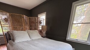 Ein Schlafzimmer mit einem großen Bett, einem Fenster, einer Wandlampe und einem dekorativen Gewebeteiler.