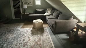 Ein Dachzimmer mit schragem Dach, einem Sofa, einem Teppich und einem an der Wand befestigten Schild.