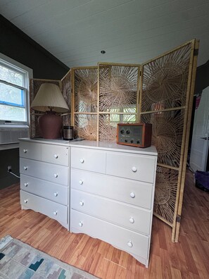 A room with a white dresser, a lamp, a radio, and a bamboo screen.