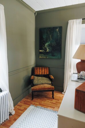 A room with a wooden floor, a chair, a painting on the wall, and a radiator.