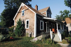 A two-story wooden house with a porch and a chimney.
