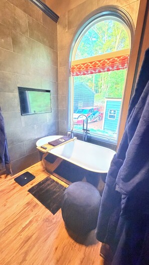 Ein Badezimmer mit einer Badewanne, einem Fenster mit Blick auf ein Haus, einem Handtuchhalter und einem Holzboden.